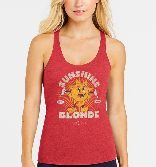 blonde woman wears red women’s racerback tank with a retro cartoon-style yellow sun character, smiling with open arms, surrounded by radiant sunbeams. The text reads ‘Sunshine Blonde’ in bold vintage Belzebuth lettering, with small details including ‘ESTD 1994’ and the RedBlonde signature logo beneath."