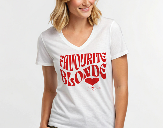 blonde woman wears a white women's loose fit v-neck graphic t-shirt with the slogan 'Favourite Blonde' in Solino Display red retro 70s wavy font. Signed with a heart and RedBlonde. Branded RedBlonde in red on inside neck and right sleeve