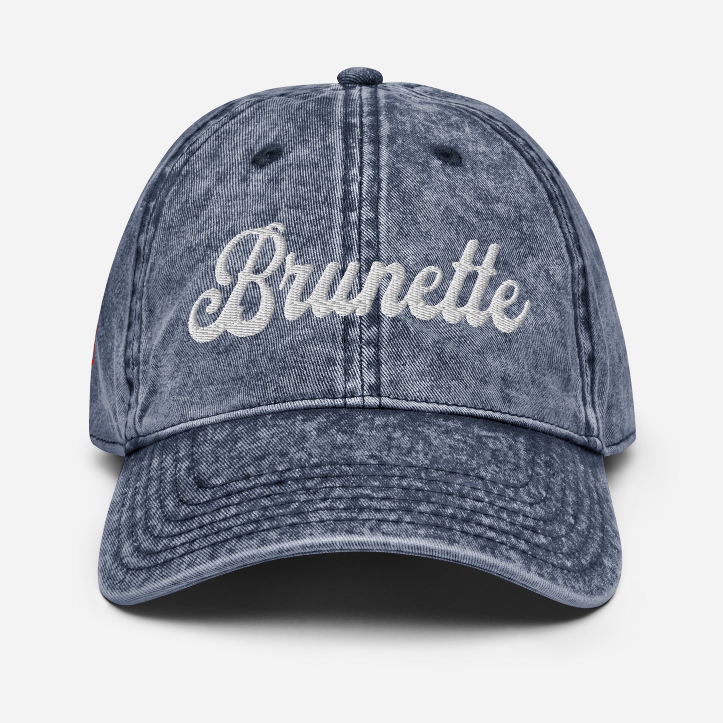 flatlay of blue denim vintage wash effect baseball cap with the word 'Brunette' embroidered on the front in white adventure font