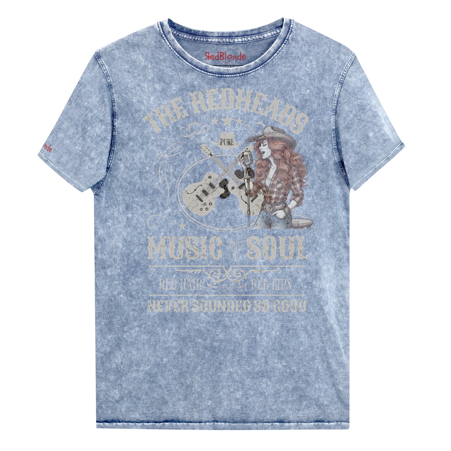 A blue denim wash unisex t-shirt with ‘THE REDHEADS’, ‘MUSIC FROM THE SOUL’, ‘RED HAIR AND RED LIPS’, and ‘NEVER SOUNDED SO GOOD’ written in Sancreek font features a graphic of a redheaded cowgirl singing with two guitars behind her. Branded RedBlonde London in red on inside neck and right sleeve