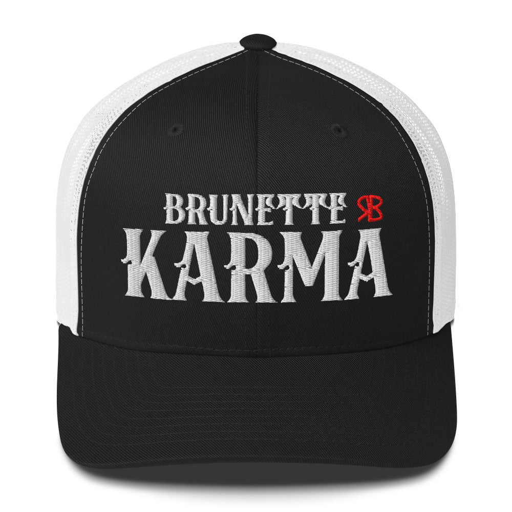 black/white retro trucker cap with mesh back. The front features bold white embroidered text reading "BRUNETTE KARMA" with a small red RB logo to the right.