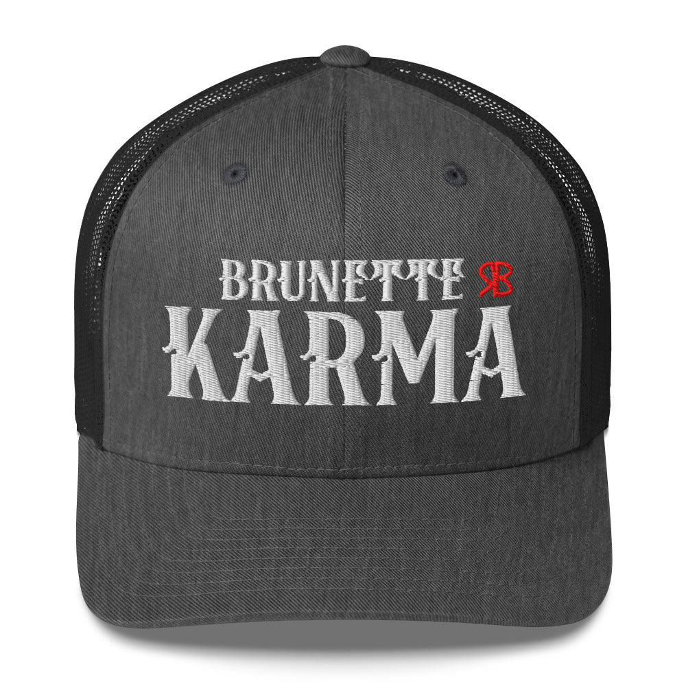 grey/black retro trucker cap with mesh back. The front features bold white embroidered text reading "BRUNETTE KARMA" with a small red RB logo to the right.