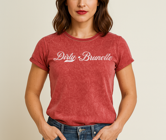 brunette wears a garnet red unisex loose-fit denim wash t-shirt with vintage Coca-Cola-inspired milkstore script in white reading ‘Dirty Brunette’ on the front. Branded RedBlonde on the inside neck and right shoulder in red