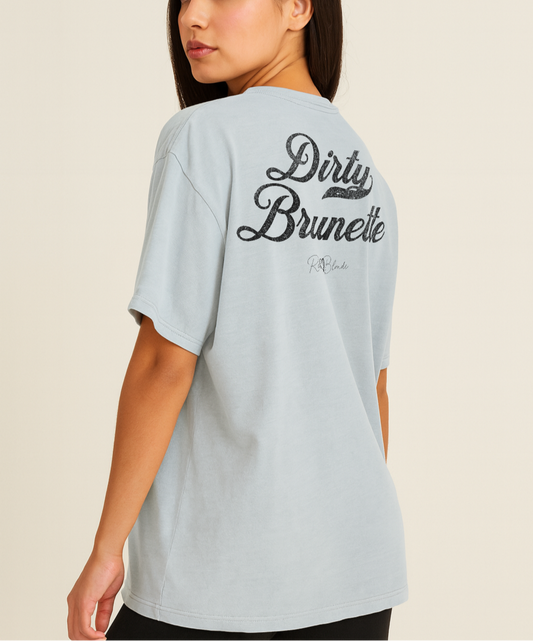 Brunette wears a pale blue vintage wash oversized unisex T-shirt with bold black Milkstore 01 vintage-style script reading “Dirty Brunette” and the RedBlonde signature logo beneath, plus a small RedBlonde logo detail on the right sleeve.
