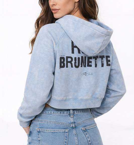 Brunette models wears a cropped snow-wash pale blue hoodie with bold black “RICH BRUNETTE” Ed Gein font and the RedBlonde signature logo printed below.