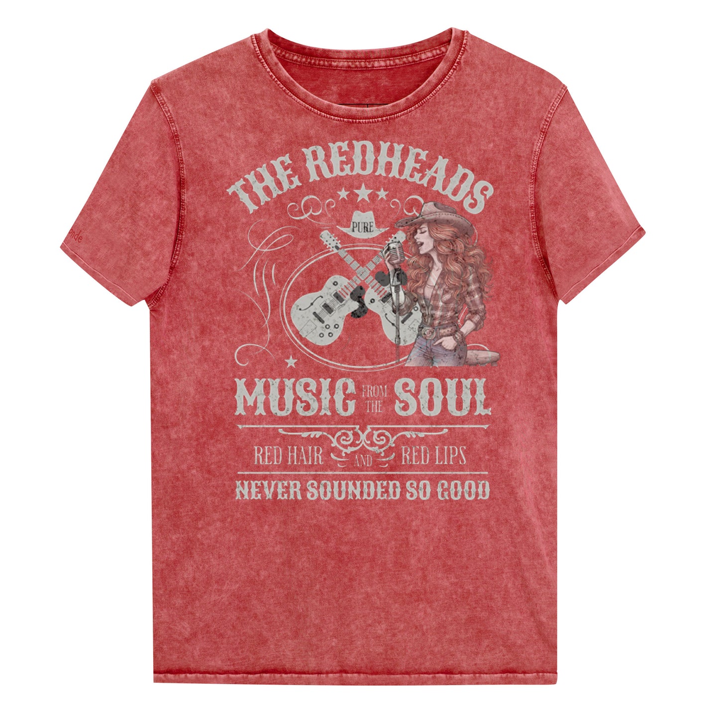 A garnet red denim wash unisex t-shirt with ‘THE REDHEADS’, ‘MUSIC FROM THE SOUL’, ‘RED HAIR AND RED LIPS’, and ‘NEVER SOUNDED SO GOOD’ written in Sancreek font features a graphic of a redheaded cowgirl singing with two guitars behind her. Branded RedBlonde London in red on inside neck and right sleeve