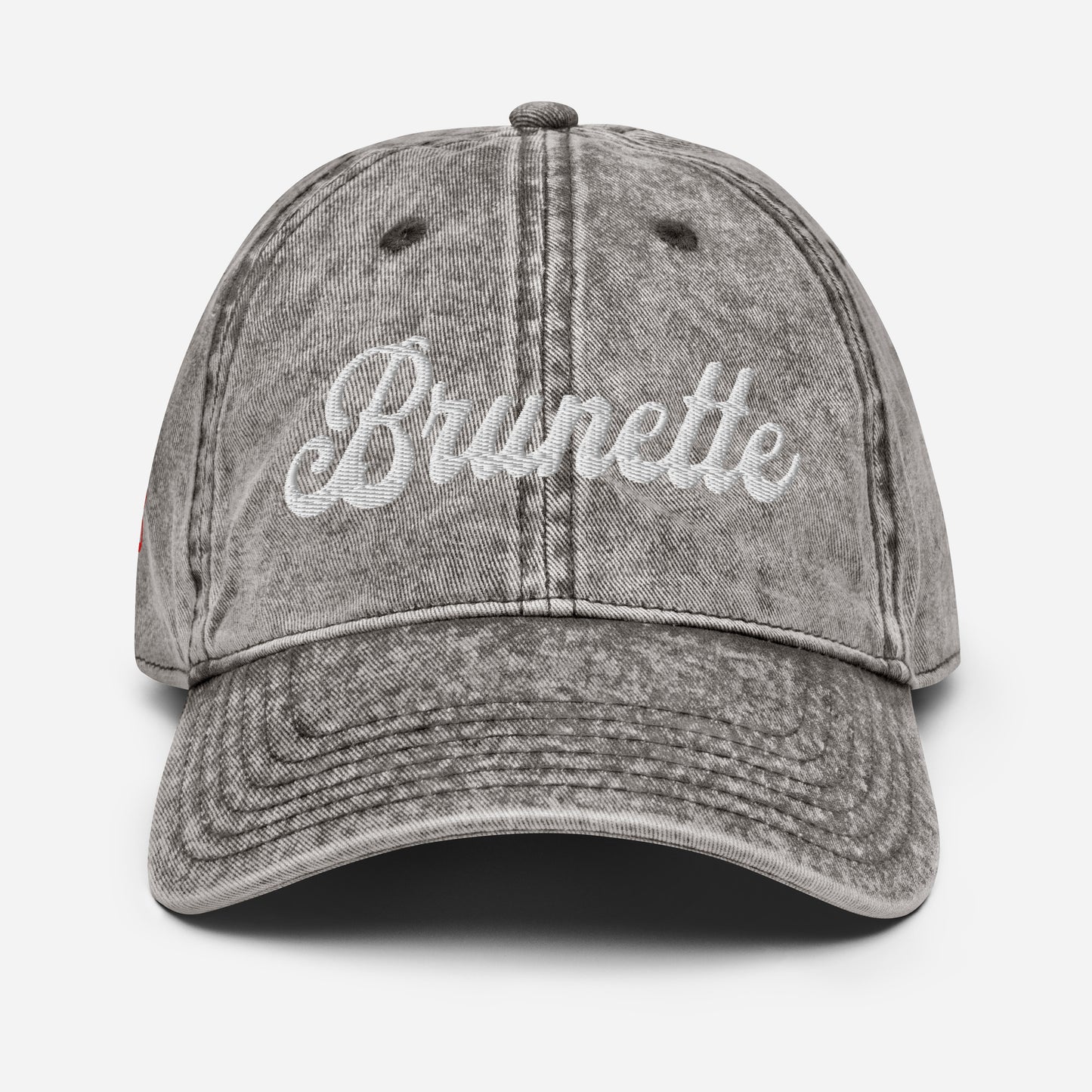 flatlay of gray denim vintage wash effect baseball cap with the word 'Brunette' embroidered on the front in white adventure font
