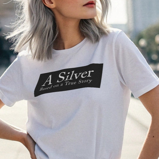 grey haired youthful model wears white unisex relaxed fit t-shirt with the slogan 'A Silver - Based on a True Story' in white text in a black box graphic. Branded RedBlonde London in red on inside neck and right sleeve