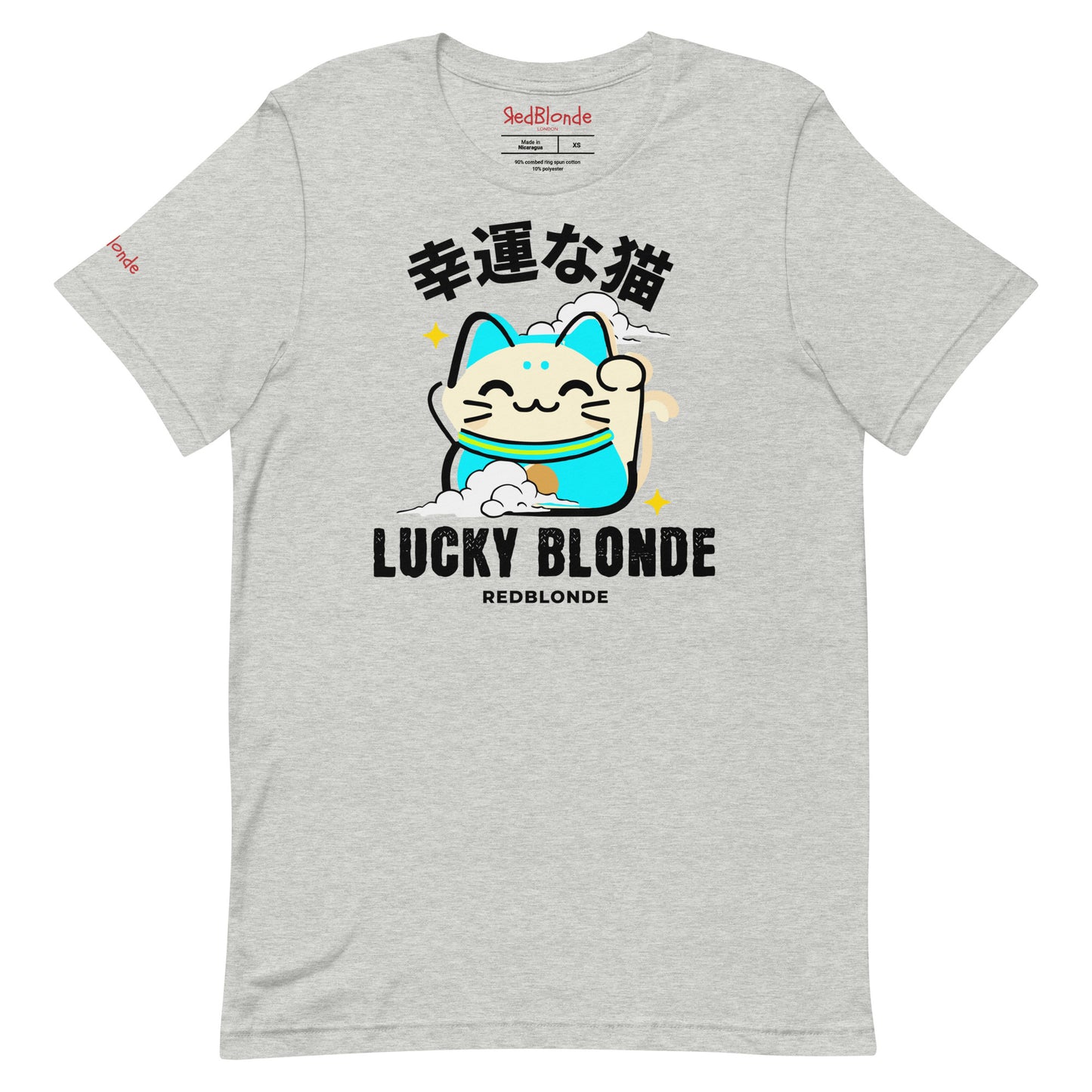 A grey unisex T-shirt featuring a cheerful maneki-neko (lucky cat) graphic in cream, turquoise, and black, with golden star accents. Above the cat are Japanese characters meaning “Lucky Cat.” Below the design, the text reads “LUCKY BLONDE” in bold black letters and “REDBLONDE” in smaller font. The T-shirt has a classic crew neckline and short sleeves. Branded RedBlonde on the inside neck and right sleeve