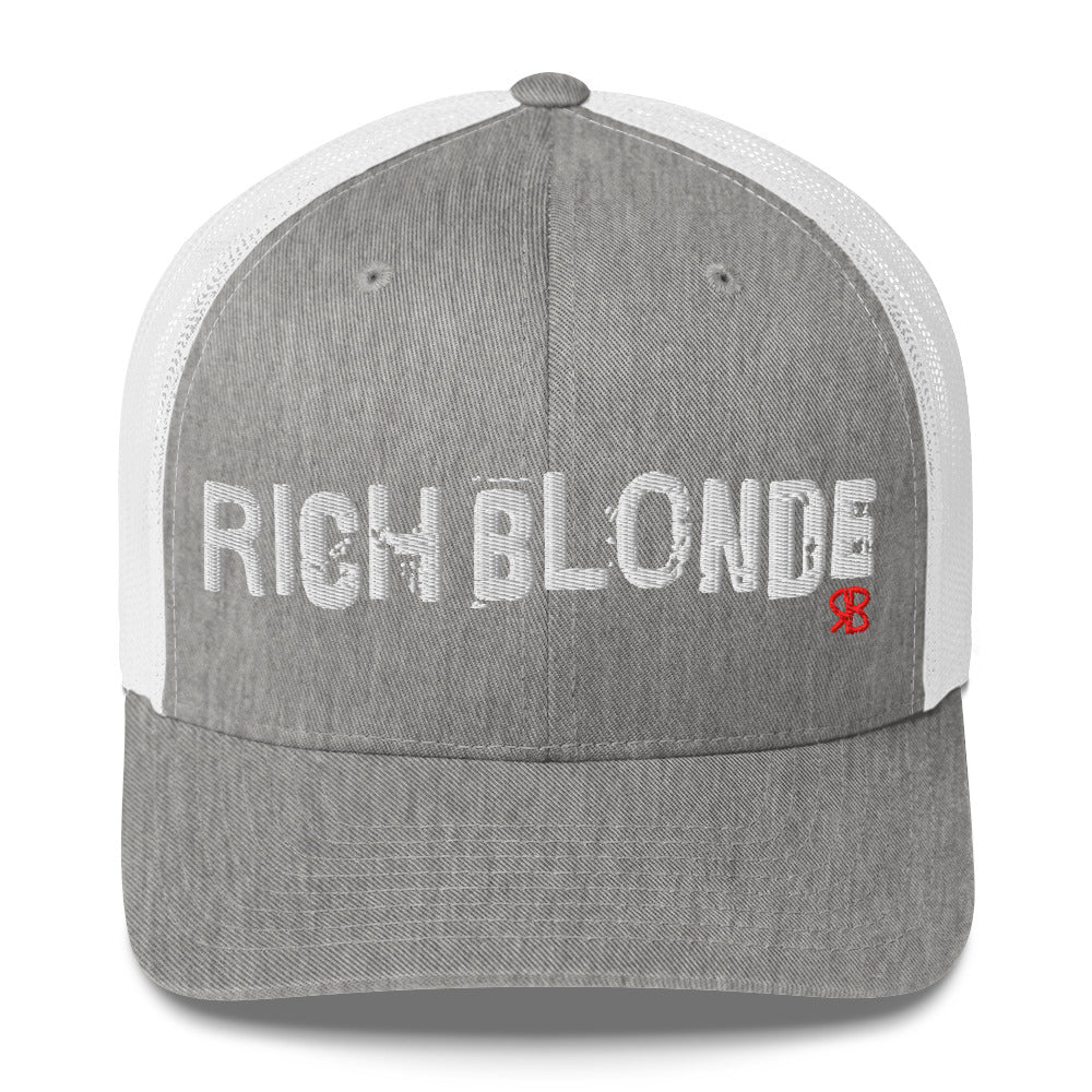 grey/white mesh-back trucker cap with the bold distressed text “RICH BLONDE” embroidered in white across the front, and a small red “RB” logo detail beneath the text. The cap has a structured front panel and curved brim