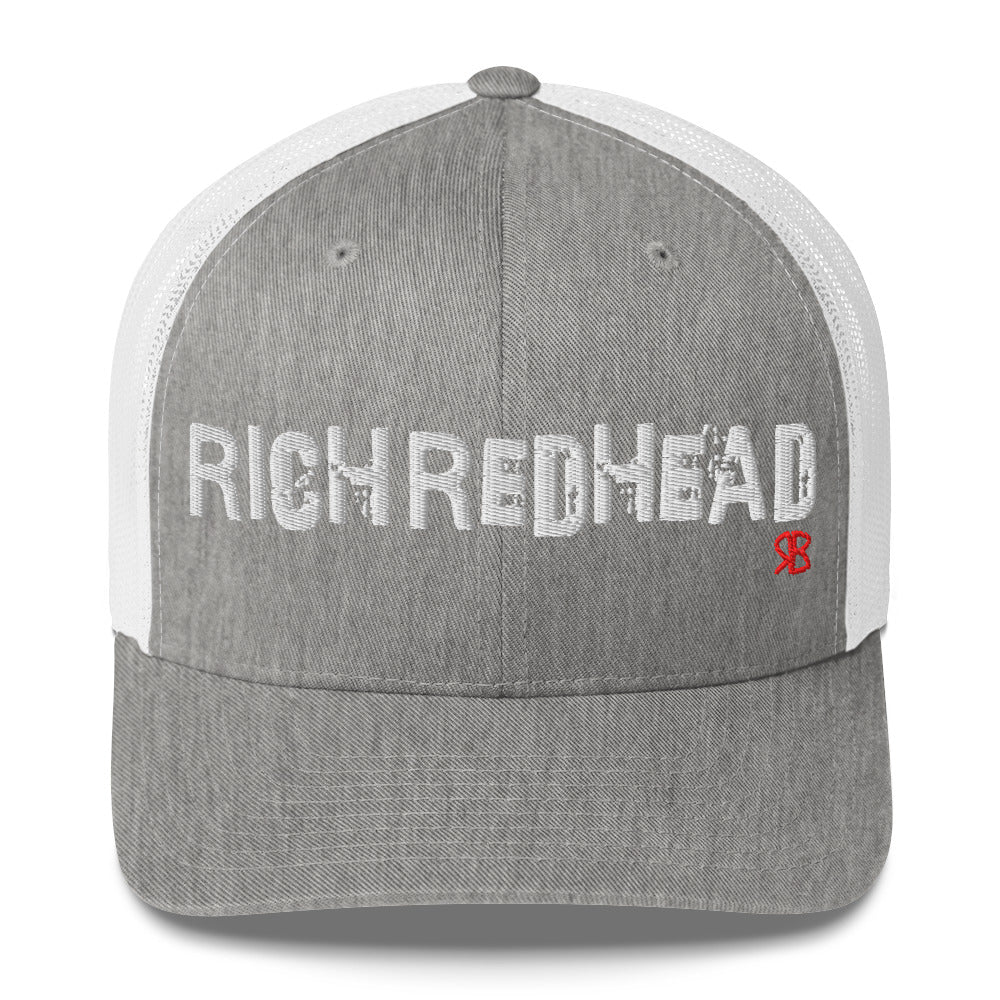 grey/white trucker cap with the bold distressed text “RICH REDHEAD” embroidered in white across the front, and a small red “RB” logo detail beneath the text. The cap has a structured front panel and curved brim