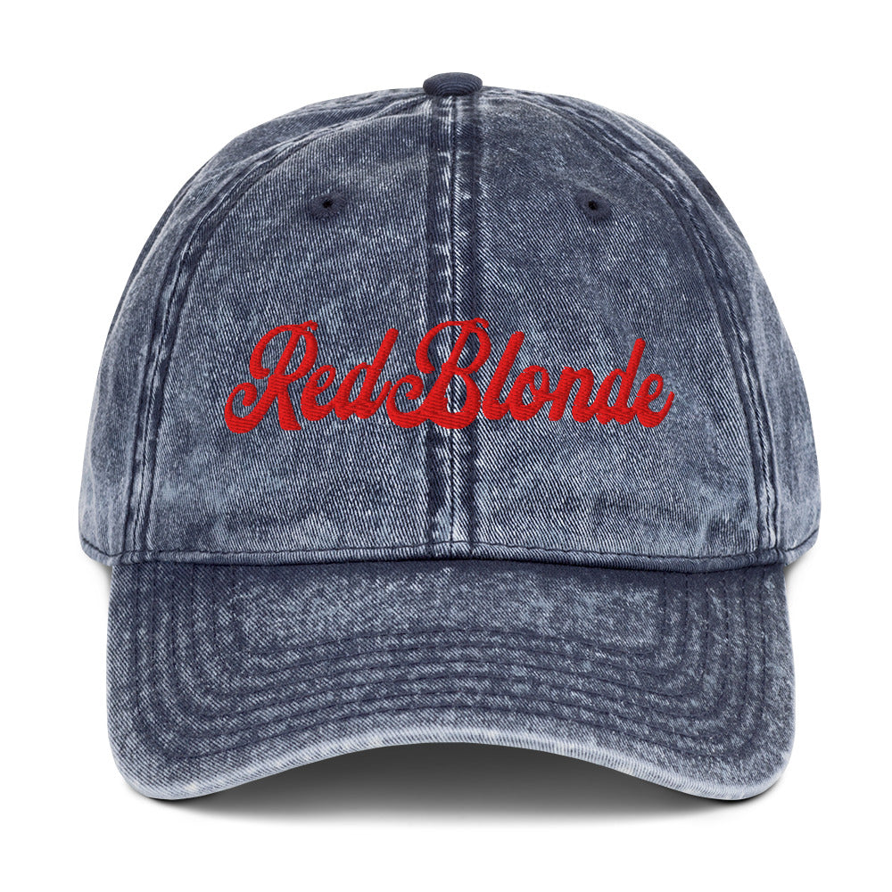 flatlay of vintage blue denim wash effect baseball cap with the word 'RedBlonde' embroidered on the front in white adventure type script font