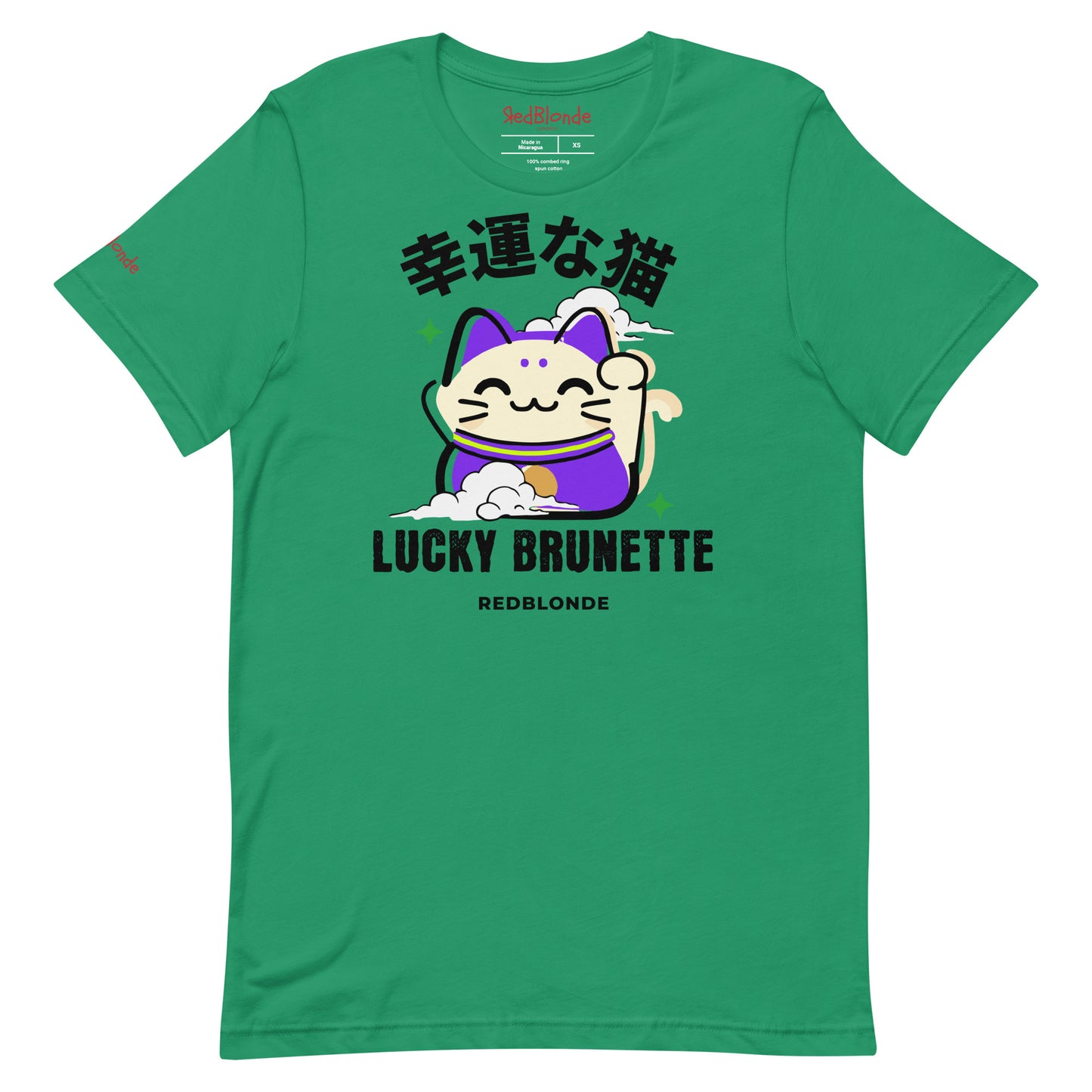 A kelly green unisex T-shirt with a classic crew neckline and short sleeves. The front features a colorful graphic of a waving Maneki-neko (lucky cat) in cream and purple, surrounded by small green sparkles. Above the cat, bold black Japanese characters are displayed. Below the cat, the text reads “LUCKY BRUNETTE” in black block letters, with “REDBLONDE” printed underneath in smaller font. Branded RedBlonde in red inside neck and right sleeve