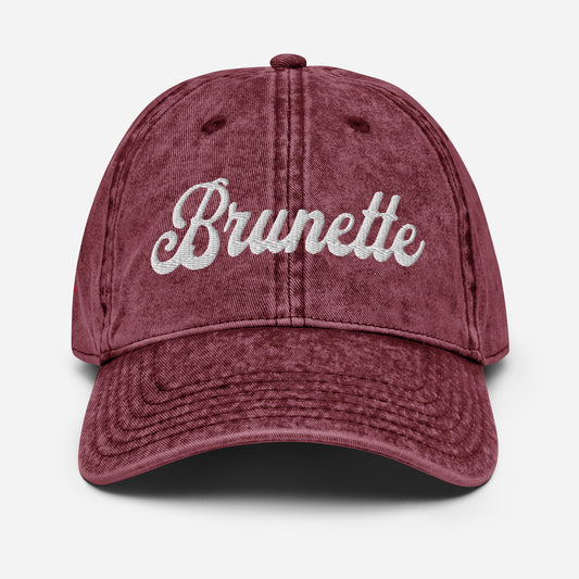 flatlay of maroon denim vintage wash effect baseball cap with the word 'Brunette' embroidered on the front in white adventure font