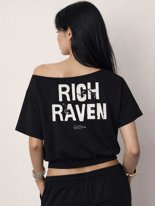 model wears a black asymmetrical shoulder t-shirt with bold white Ed Gein font “RICH RAVEN" slogan on the front and RedBlonde logo beneath.