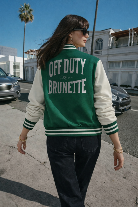 model wears a Green & white varsity-style jacket with cream sleeves and striped ribbed trims. The back features large white text reading “OFF DUTY BRUNETTE” in Brookfield font with a small RedBlonde signature logo in the centre between the words