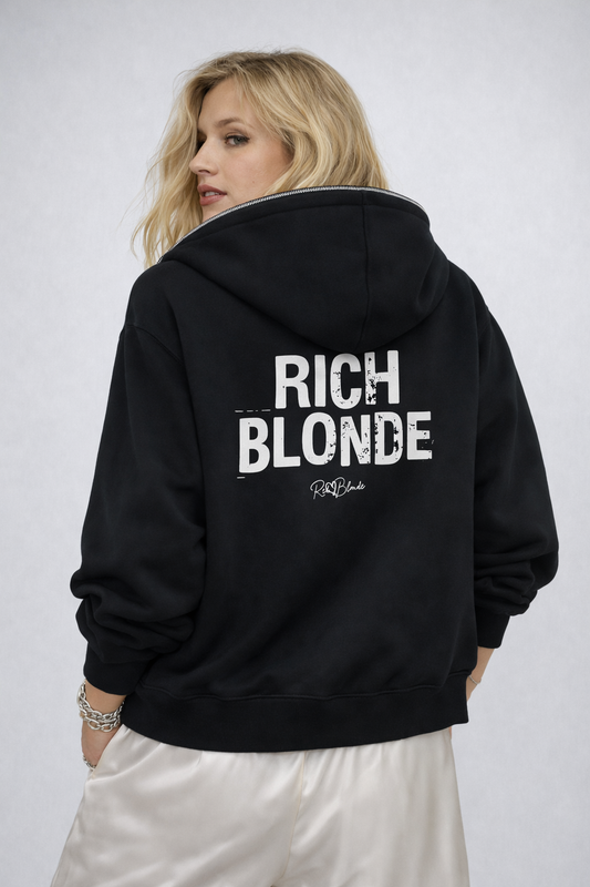 model wears a Black hem to hood zip-up hoodie with cropped oversized fit and ribbed cuffs/hem, featuring large distressed white “RICH BLONDE” Ed Gein text across the back with a small “RedBlonde” script logo beneath.