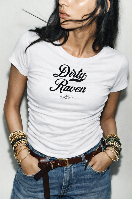 model wears a short-sleeve white crewneck T-shirt laid flat on a white background. It has subtle ruching/contouring at the sides and a slightly curved hem. black script text across the chest reads “Dirty Raven,” in Milkstore 01 script with a small cursive “RedBlonde” logo beneath.