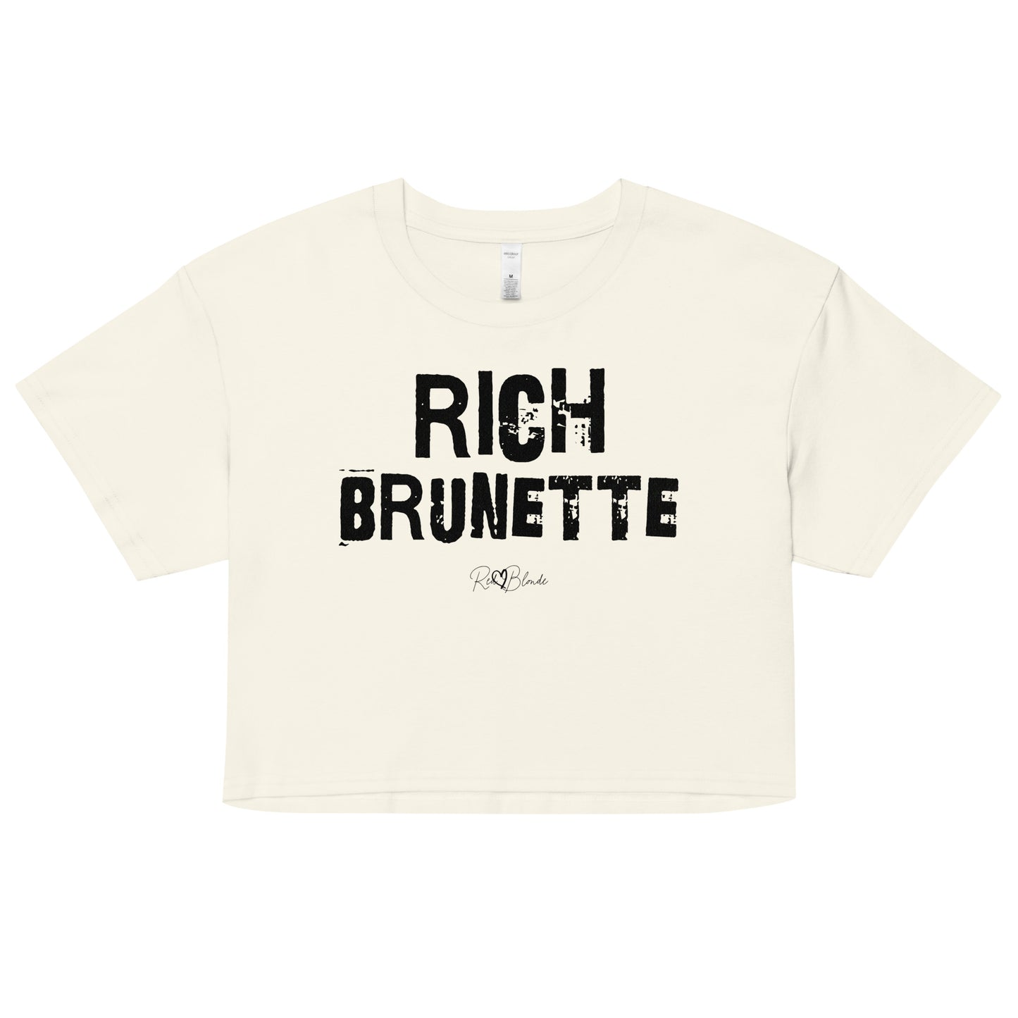 a natural coloured crop top with a relaxed fit, short sleeves, and a wide crew neckline. The front features bold black distressed Ed Gein lettering reading “RICH BRUNETTE” with the RedBlonde signature logo underneath in black