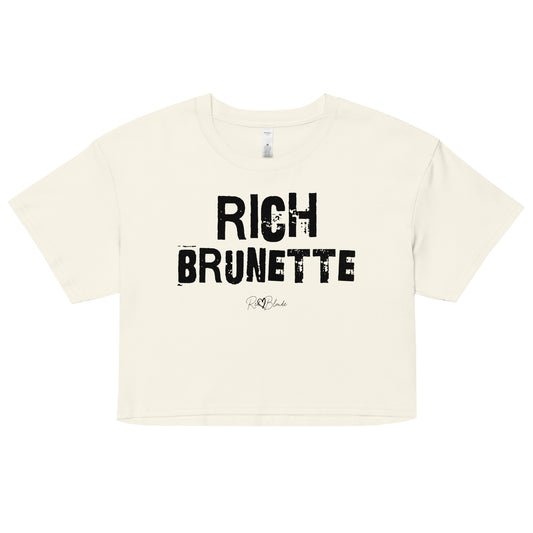a natural coloured crop top with a relaxed fit, short sleeves, and a wide crew neckline. The front features bold black distressed Ed Gein lettering reading “RICH BRUNETTE” with the RedBlonde signature logo underneath in black