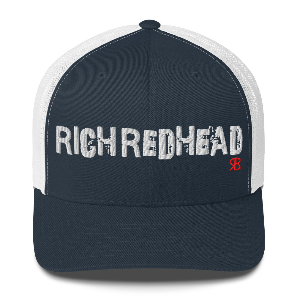navy/white trucker cap with the bold distressed text “RICH REDHEAD” embroidered in white across the front, and a small red “RB” logo detail beneath the text. The cap has a structured front panel and curved brim
