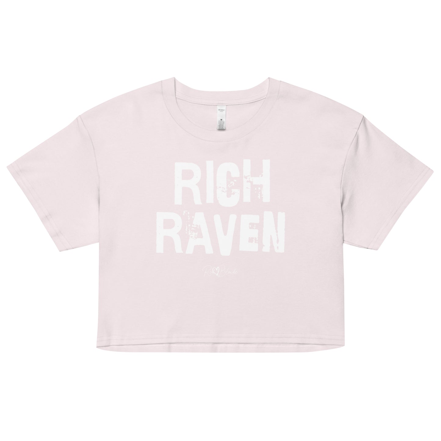 an orchid coloured crop top with a relaxed fit, short sleeves, and a wide crew neckline. The front features bold white distressed lettering reading “RICH RAVEN” with the RedBlonde signature logo underneath in white