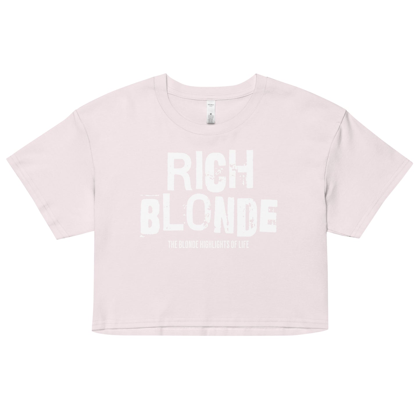 An orchid women’s crop top with a relaxed fit, short sleeves, and a wide crew neckline. The front features bold white distressed lettering reading “RICH BLONDE” with the tagline “THE BLONDE HIGHLIGHTS OF LIFE” in smaller text below.