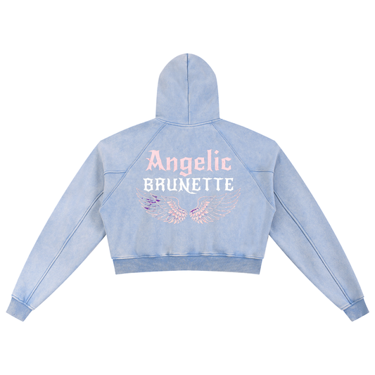 Back view of a pale blue cropped hoodie with hood up, featuring “Angelic Brunette” New Rocker font text and iridescent angel wings graphic printed across the back on a white background.