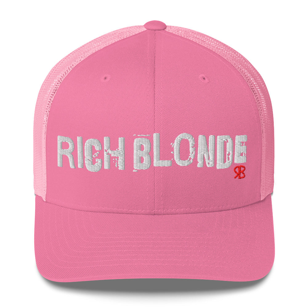pink mesh-back trucker cap with the bold distressed text “RICH BLONDE” embroidered in white across the front, and a small red “RB” logo detail beneath the text. The cap has a structured front panel and curved brim