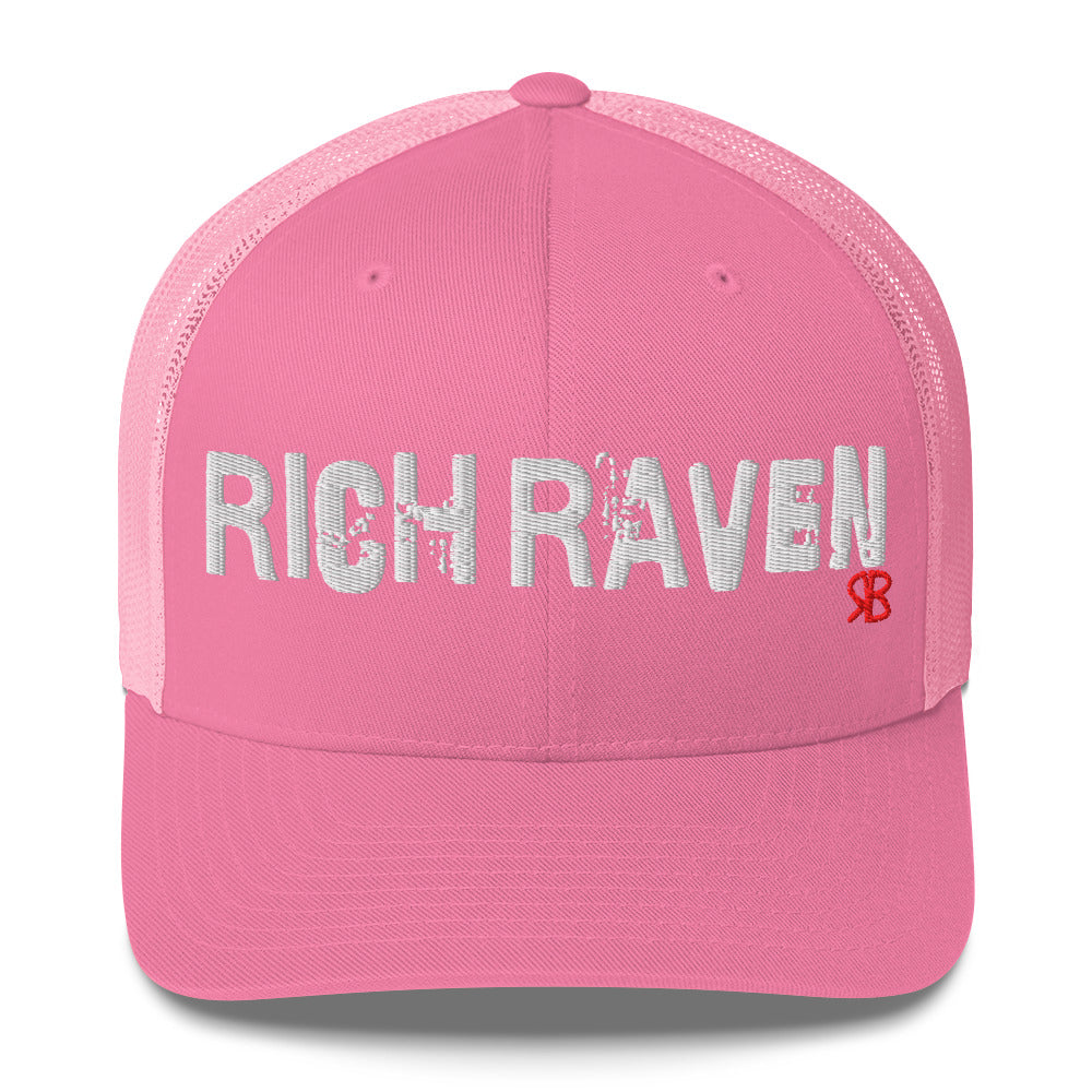pink mesh-back trucker cap with the bold distressed text “RICH RAVEN” embroidered in white across the front, and a small red “RB” logo detail beneath the text. The cap has a structured front panel and curved brim