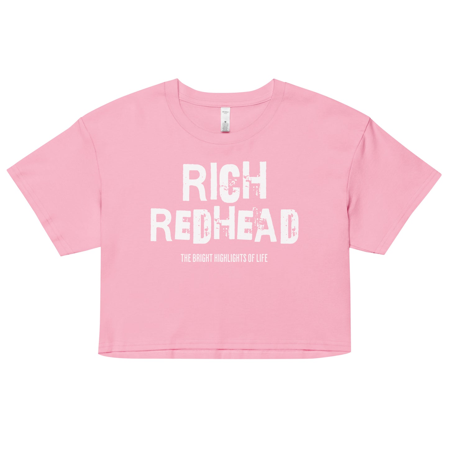 A pink women’s crop top with a relaxed fit, short sleeves, and a wide crew neckline. The front features bold black distressed lettering reading “RICH REDHEAD” with the tagline “THE BRIGHT HIGHLIGHTS OF LIFE” in smaller text below.