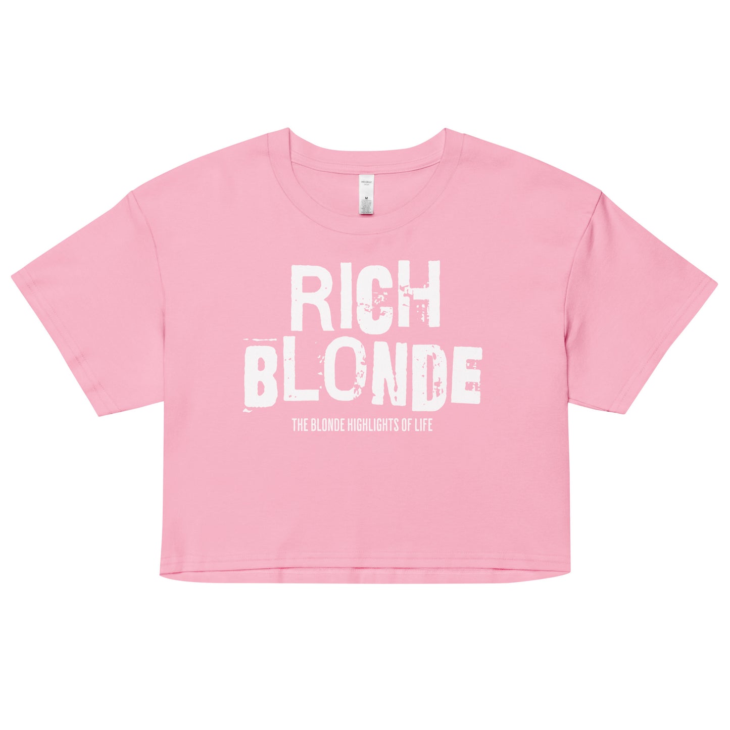 A pink women’s crop top with a relaxed fit, short sleeves, and a wide crew neckline. The front features bold white distressed lettering reading “RICH BLONDE” with the tagline “THE BLONDE HIGHLIGHTS OF LIFE” in smaller text below.