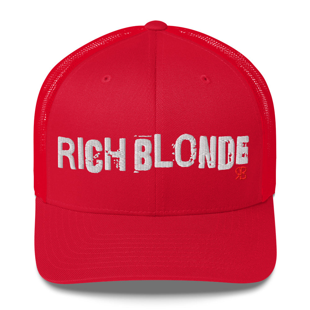 red mesh-back trucker cap with the bold distressed text “RICH BLONDE” embroidered in white across the front, and a small red “RB” logo detail beneath the text. The cap has a structured front panel and curved brim
