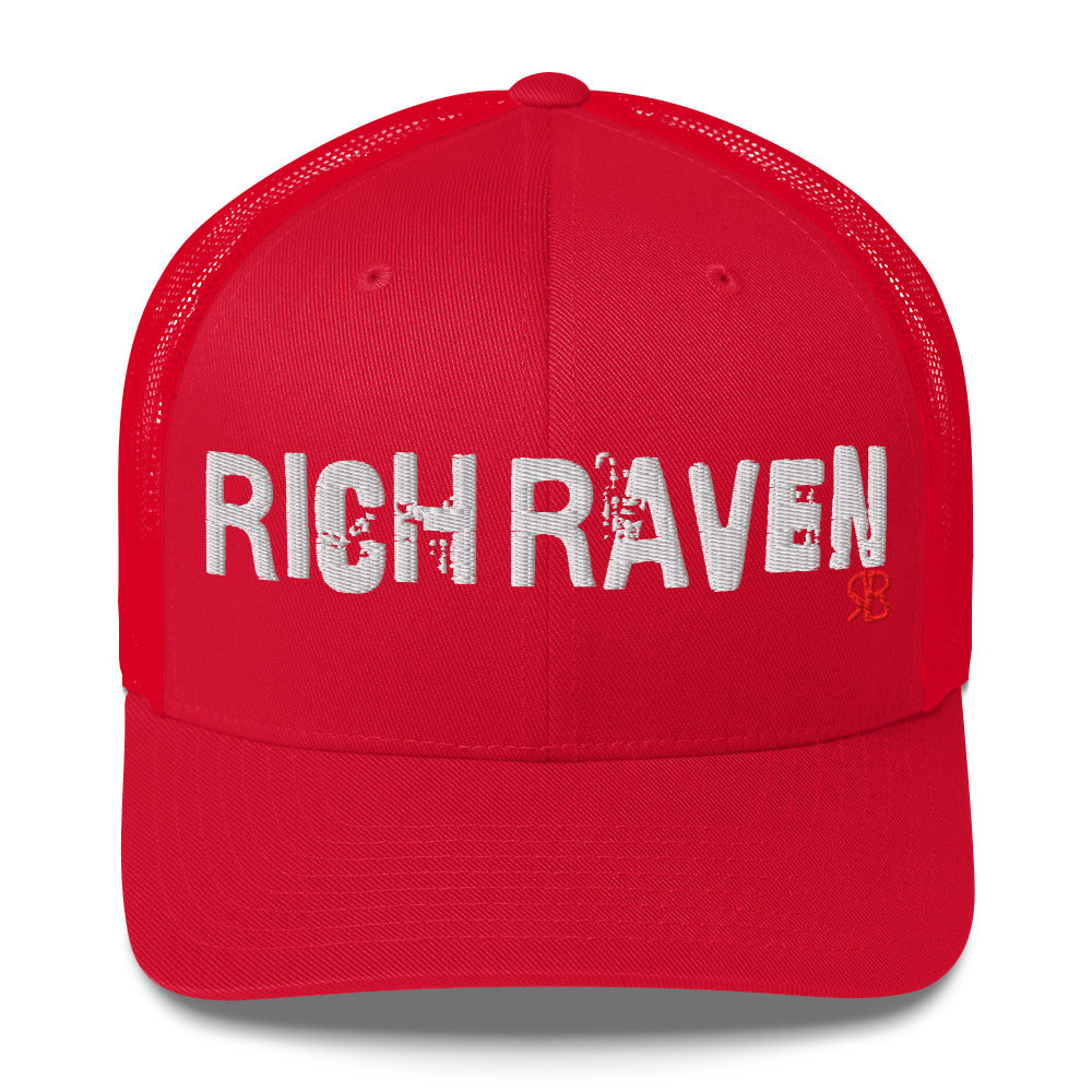 red mesh-back trucker cap with the bold distressed text “RICH RAVEN” embroidered in white across the front, and a small red “RB” logo detail beneath the text. The cap has a structured front panel and curved brim