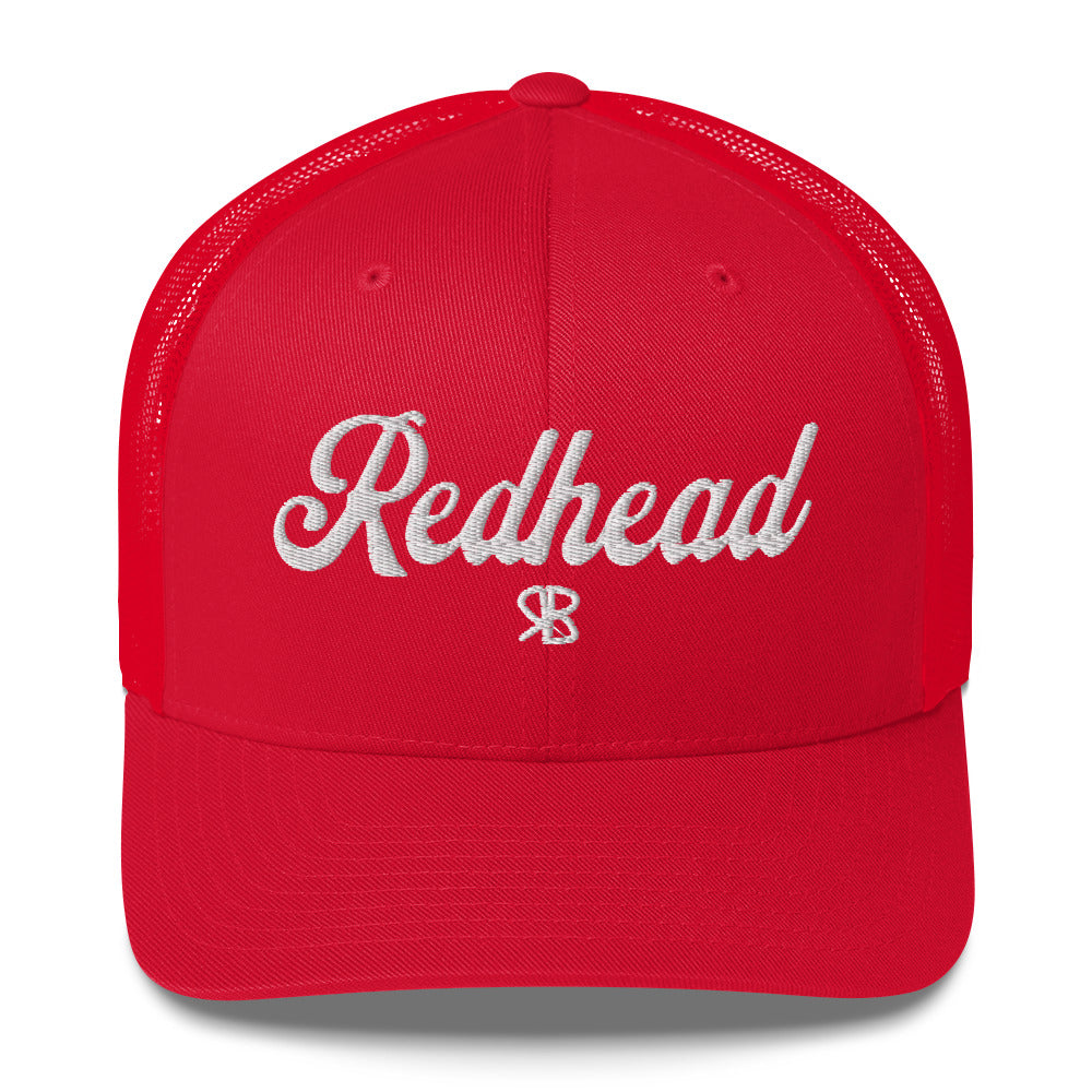 red trucker cap with 'Redhead' in white adventurer 01 font on front. Mesh back. Branded RB