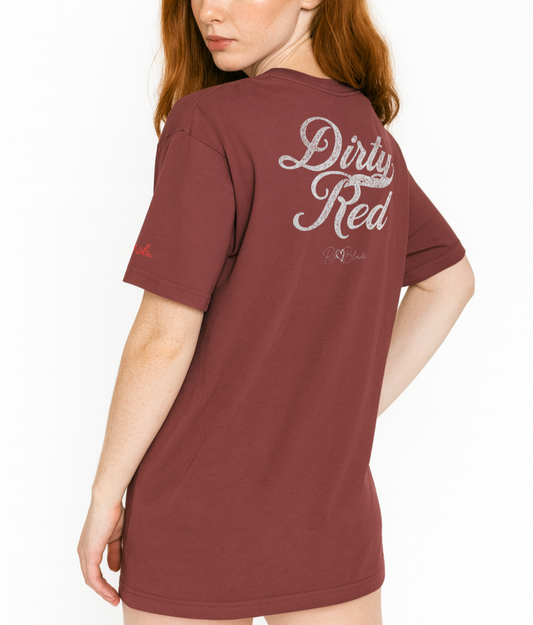 redhead wears maroon vintage wash oversized unisex T-shirt with bold white Milkstore 01 vintage-style script reading “Dirty Red” and the RedBlonde signature logo beneath, plus a small RedBlonde logo detail on the right sleeve.