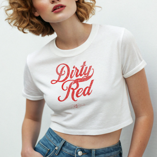 redhead wears a white women’s crop top featuring the phrase “Dirty Red” in bold, red milkstore vintage-style script across the chest. Below the phrase, the brand name “RedBlonde” is printed in a smaller, elegant handwritten font.