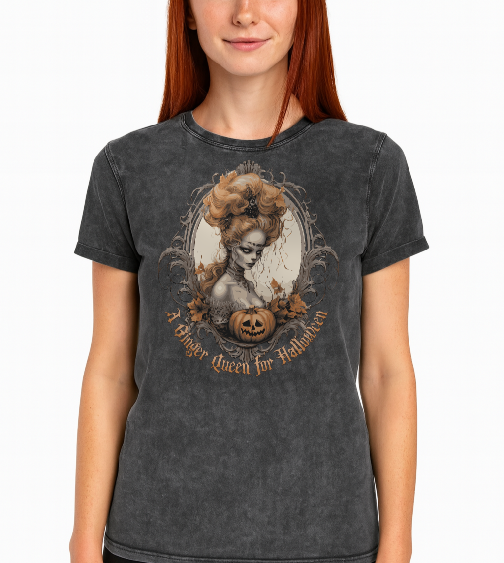 redhead ginger woman wears a Black acid-wash unisex T-shirt featuring a gothic-style illustration of ginger-haired woman with an elaborate beehive hairstyle, framed by ornate scrollwork, autumn leaves, and a carved pumpkin. The design is captioned with the text ‘A Blonde Queen for Halloween’ in vintage Dark Angle lettering. Branded RedBlonde in red on inside neck and right sleeve