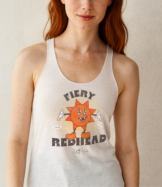 Redhead wears a White women’s racerback tank with a bold retro graphic of a smiling orange cartoon sun character, surrounded by radiant sunbeams. The text reads ‘Fiery Redhead’ in distressed black Belzebuth lettering with small details including ‘ESTD 1994’ and the RedBlonde signature logo beneath."