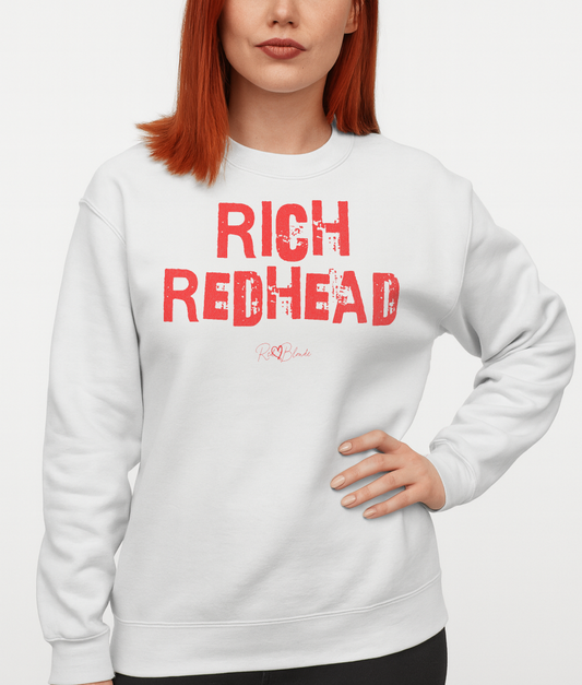 Redhead wears white unisex premium sweatshirt with bold distressed white Ed Geinitext “RICH REDHEAD” on the front, featuring a subtle RedBlonde logo beneath the lettering and on the sleeve cuff and inside neck