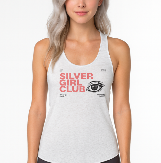 silver haired model wears Heather white women’s racerback tank top featuring the text “SILVER GIRL CLUB” in bold pink DT Getai Grotesh text across the chest, paired with a stylized black eye graphic. Smaller black text reads “Brains First,” “Shimmer Always,” “ESTD 2025,” and “Born to be Bold.”