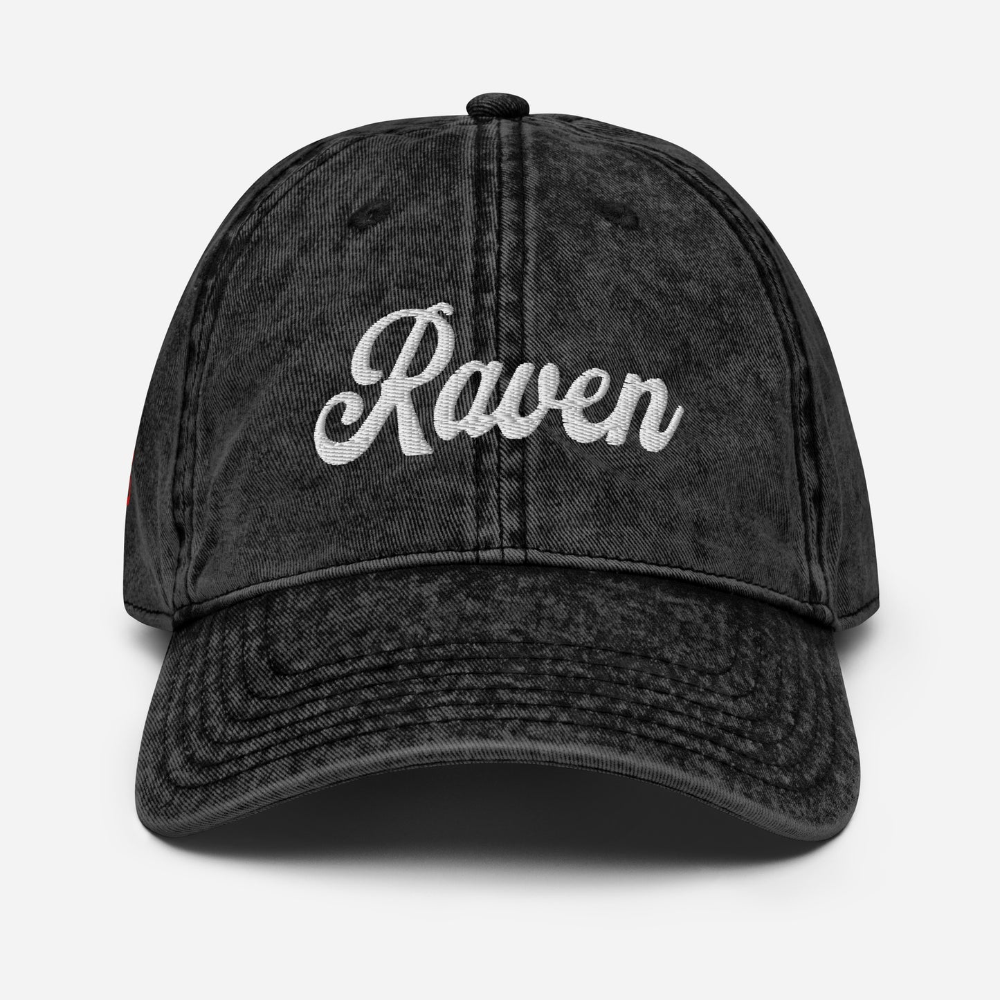 flatlay of vintage black denim wash effect baseball cap with the word 'Raven' embroidered on the front in white adventure type script font