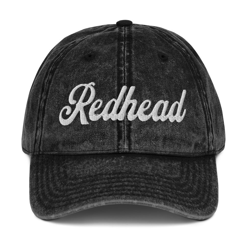 flatlay of vintage black denim wash effect baseball cap with the word 'Redhead' embroidered on the front in white adventure type script font