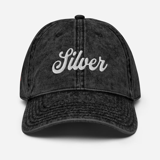 flatlay of vintage black denim wash effect baseball cap with the word 'Silver' embroidered on the front in white adventure type script font