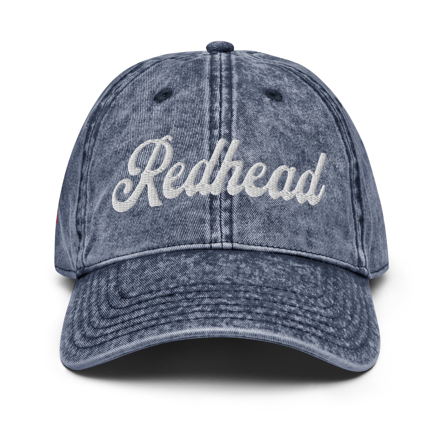 flatlay of vintage blue denim wash effect baseball cap with the word 'Redhead' embroidered on the front in white adventure type script font
