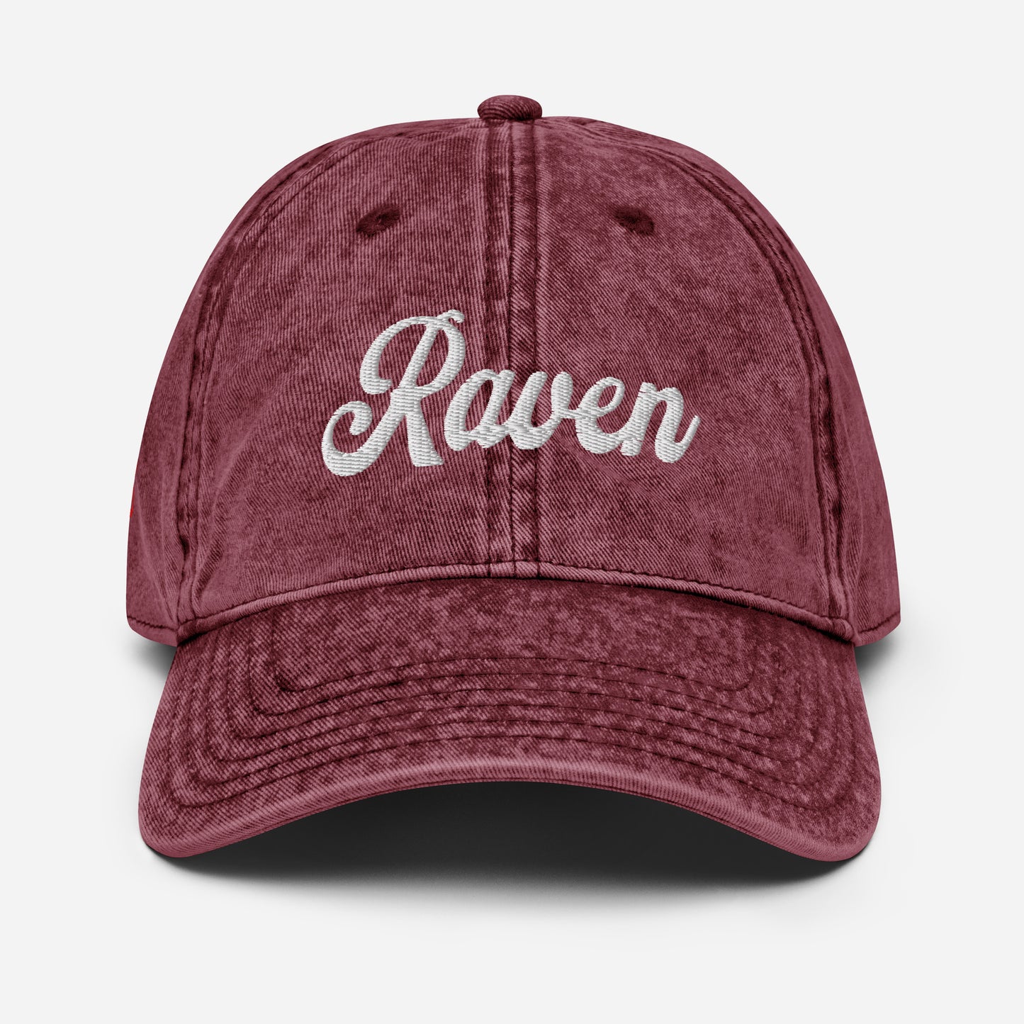 flatlay of vintage maroon denim wash effect baseball cap with the word 'Raven' embroidered on the front in white adventure type script font