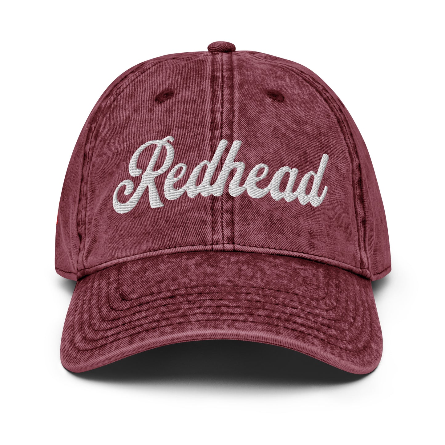 flatlay of vintage maroon denim wash effect baseball cap with the word 'Redhead' embroidered on the front in white adventure type script font
