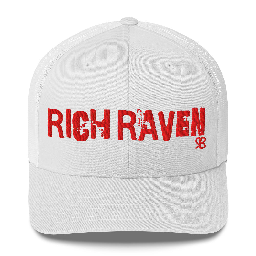 white mesh-back trucker cap with the bold distressed text “RICH RAVEN” embroidered in red across the front, and a small red “RB” logo detail beneath the text. The cap has a structured front panel and curved brim