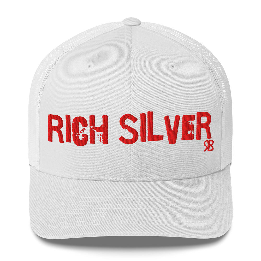 white mesh-back trucker cap with the bold distressed text “RICH SILVER” embroidered in red across the front, and a small red “RB” logo detail beneath the text. The cap has a structured front panel and curved brim
