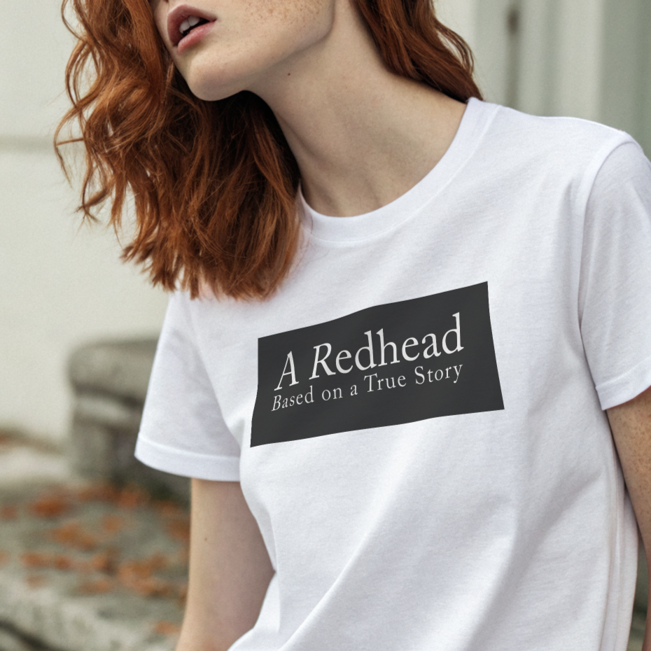 redhead model, by stone steps, wears a white unisex relaxed fit t-shirt with the slogan 'A Redhead. Based on a True Story' in white text in a black box graphic